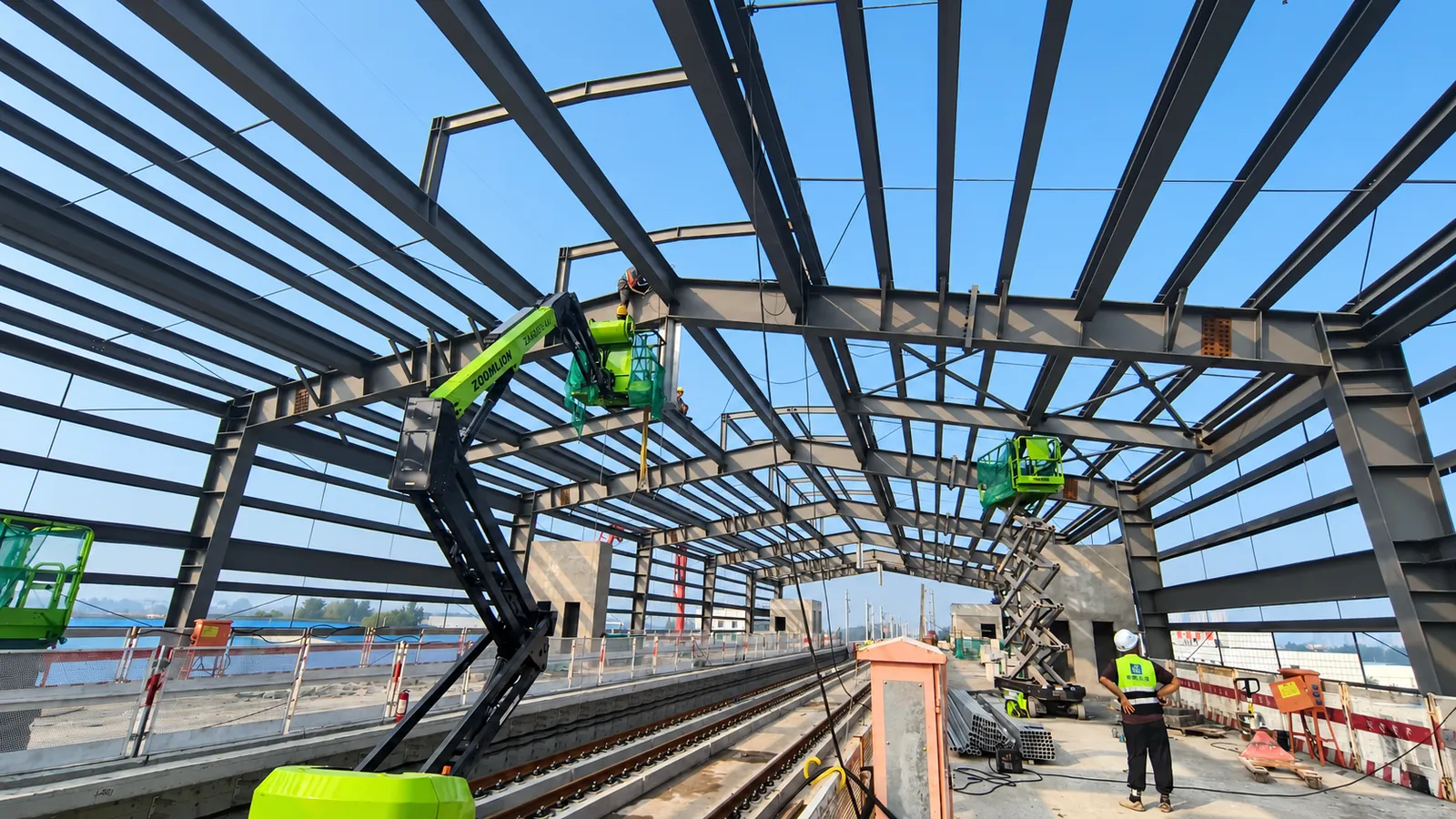 Workers on boom lifts connecting purlins to the station frames